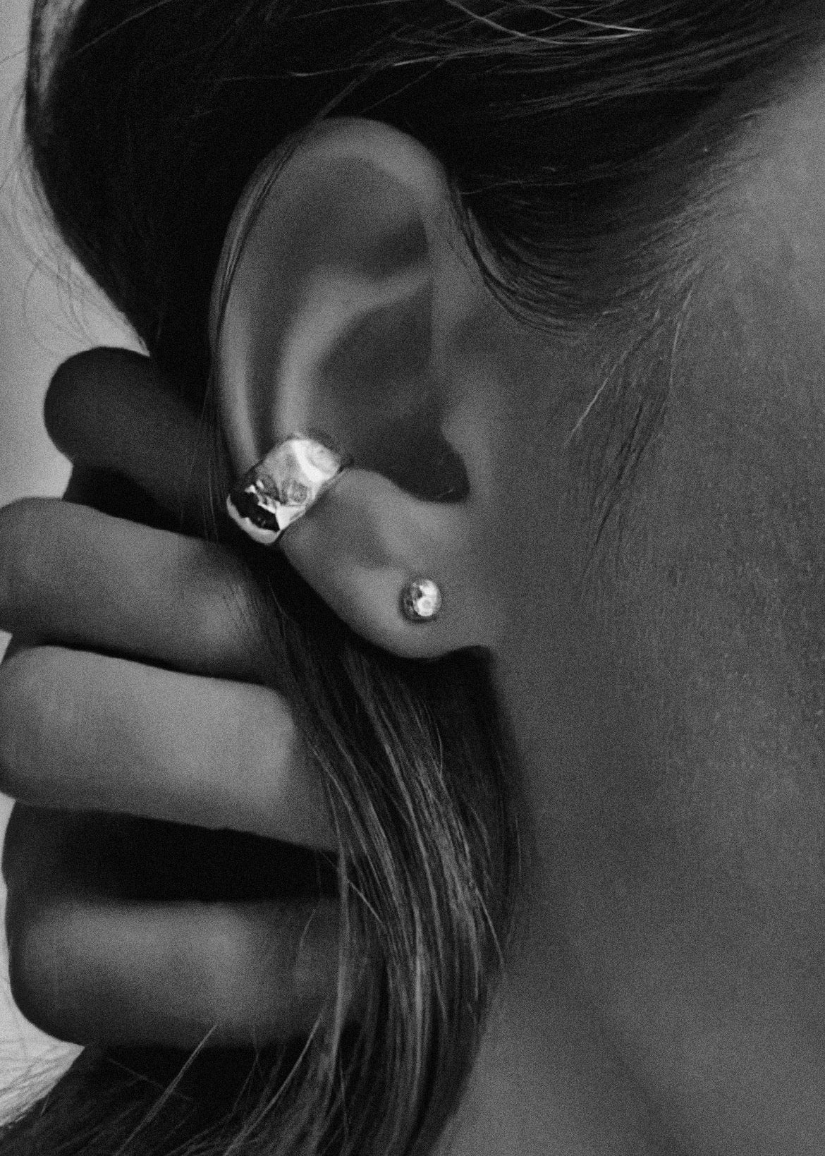 Close-up of an ear wearing a silver stud earring and a silver ear cuff