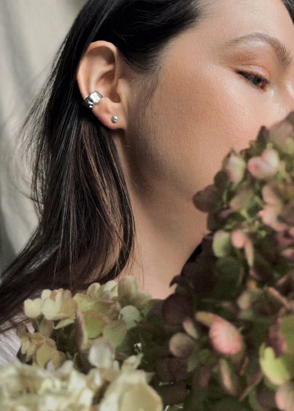 Person with floral arrangement, wearing a stud earring and an ear cuff made in silver