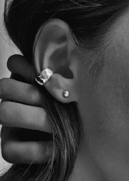 Close-up of an ear wearing a silver stud earring and a silver ear cuff