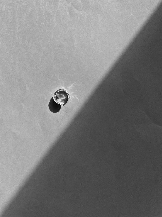 Close-up of a silver ear cuff on a textured gray surface with a shadow.